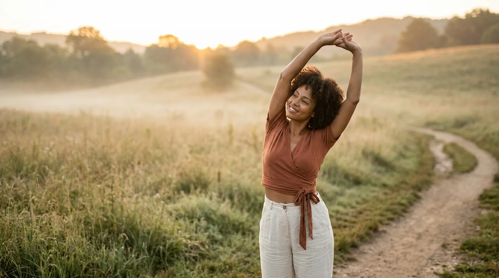 A woman stretching with her arms overhead in a misty golden meadow at sunrise